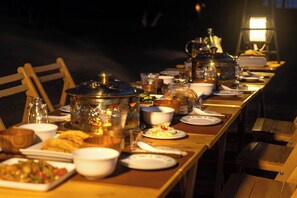 Una mesa de comedor dispuesta con diversos platos, vasos y una tetera, iluminada por una lámpara.