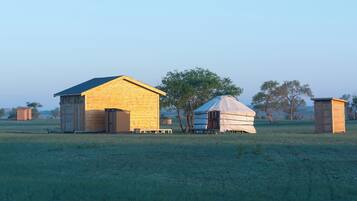 A rustic wooden building with a sloped roof, a small wooden structure with a flat roof, and a large tent-like structure in a grassy field.