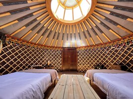 Interior de una yurta con dos camas, una mesa de madera y un tragaluz central.