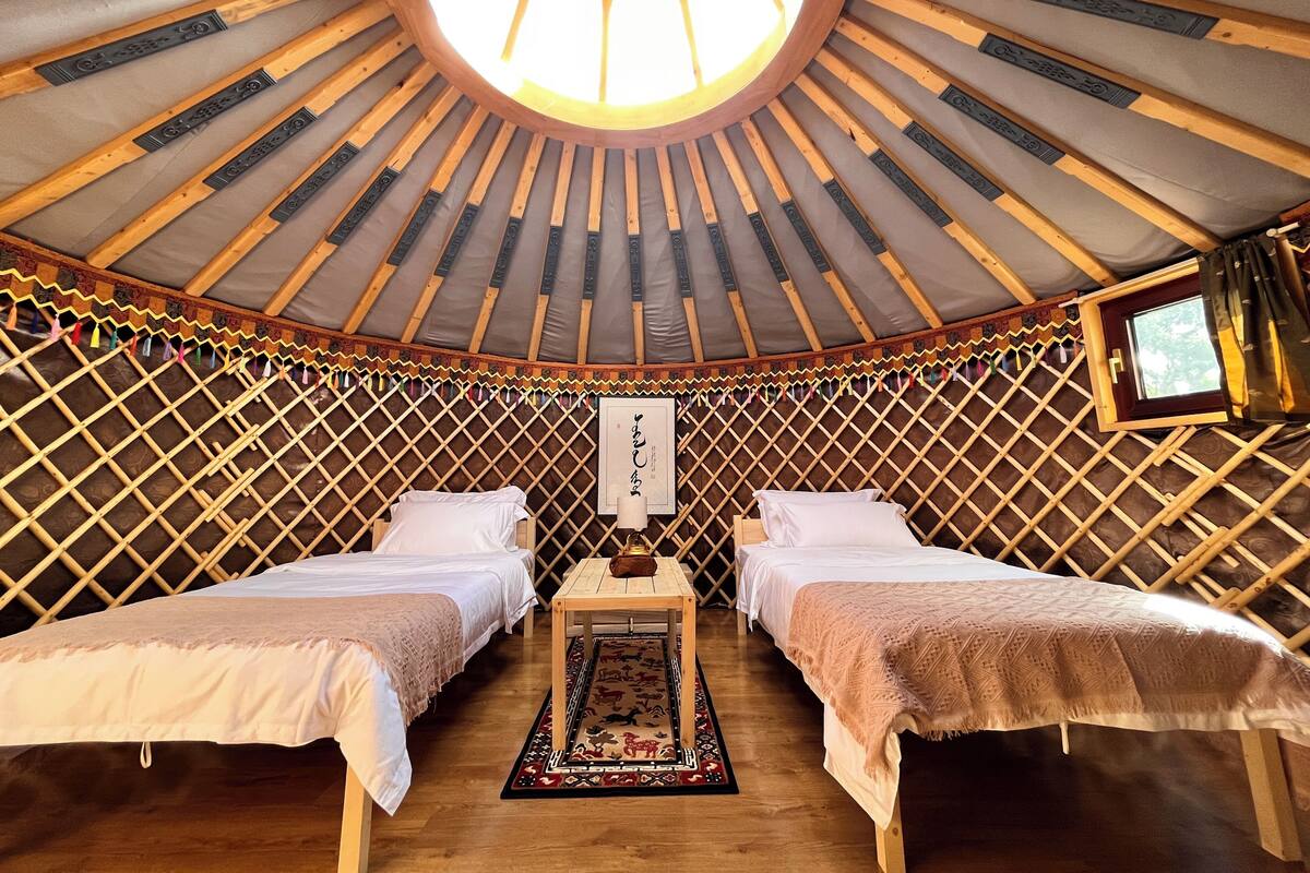 A yurt with two beds, a central table, and a decorative rug.
