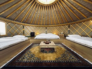 Interior de una yurtas tradicional con tres camas, una mesa de madera en el centro y una alfombra estampada.