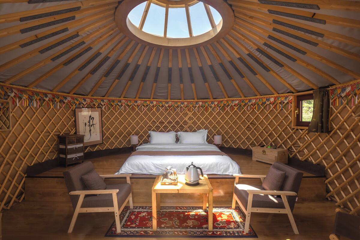 A yurt with a bed, two chairs, a table, and a decorative rug.