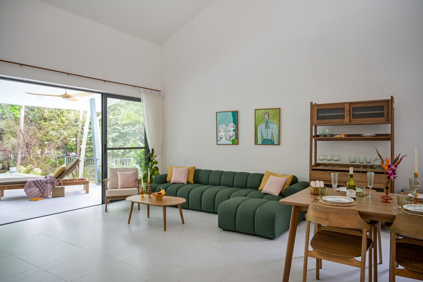 Un salon moderne avec un canapé d’angle vert, une table à manger en bois pour quatre personnes et une grande porte-fenêtre coulissante donnant sur un balcon.