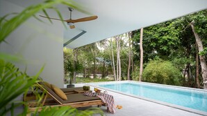 A modern poolside area with a wooden lounge chair, a ceiling fan, and a view of a swimming pool surrounded by lush greenery. - Zen Paradise Pool Villa by Sea N' Rent (Ko Pha-ngan)