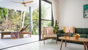 A modern living room with a green sofa, a wooden coffee table with candles, a lounge chair, and a view of lush greenery outside. - Zen Paradise Pool Villa by Sea N' Rent (Ko Pha-ngan)