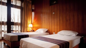 Hotellihuone, jossa on kaksi erillistä sänkyä, puuseinät, ikkuna, jossa on verhot, ja yöpöytälamppu.