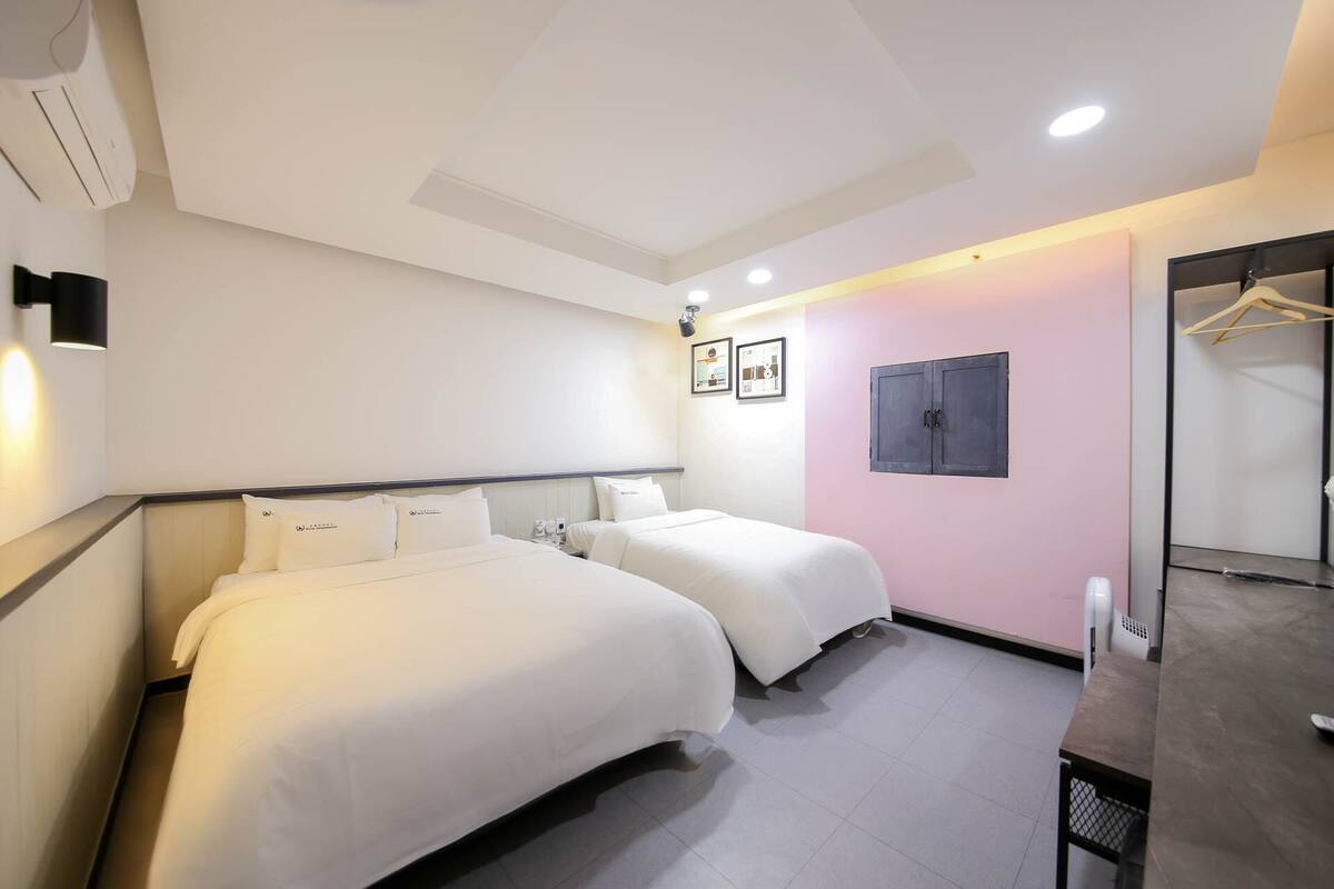 A hotel room with two beds, a wardrobe, a desk, and a mirror.