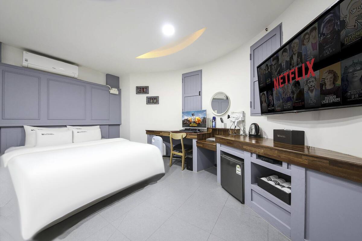 A modern bedroom with a bed, desk, and a wall-mounted TV displaying Netflix content.