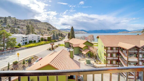 Ein Hotel mit grüner und brauner Fassade, einem Parkplatz und Blick auf Berge und See.