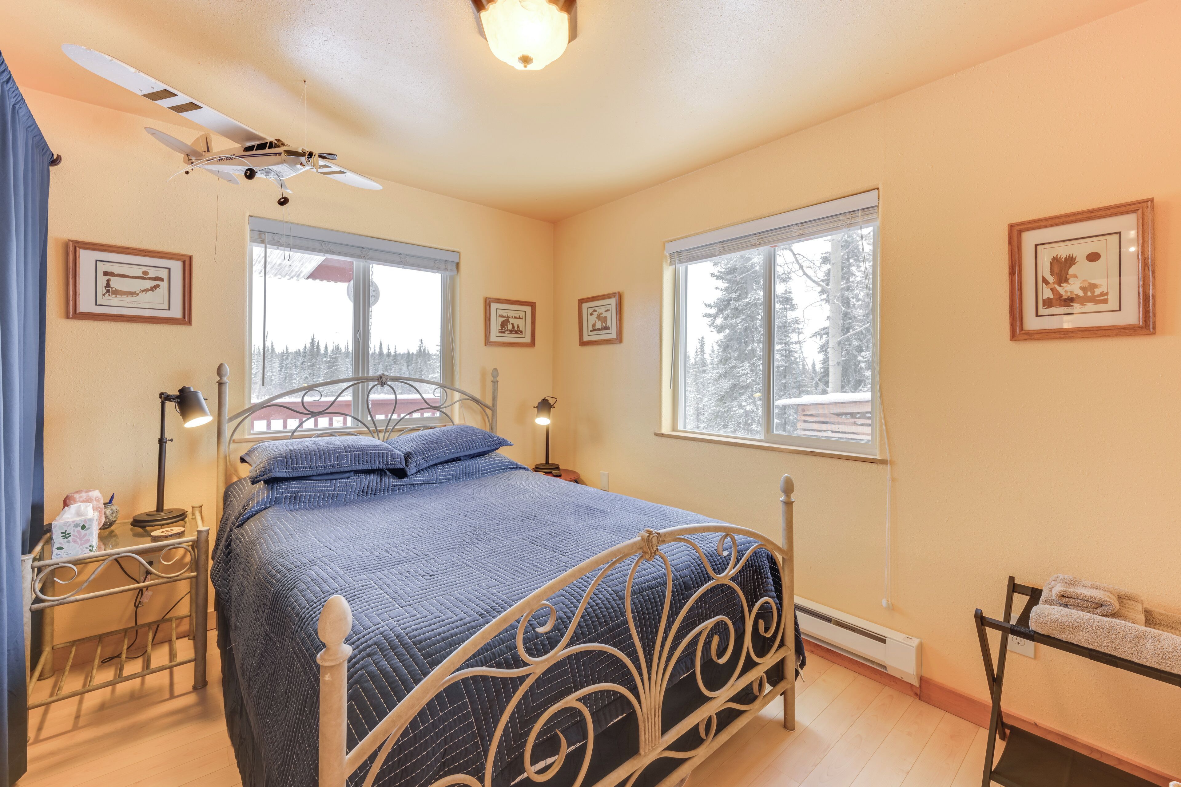 A bedroom with a bed, a window with a view of trees, a ceiling fan, and a framed picture on the wall.