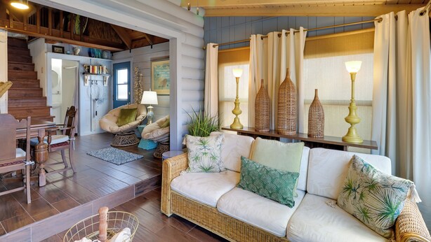 A cozy living room with a wicker sofa, a dining area with wooden furniture, and a staircase leading to another level. - Fish On-Site: Okeechobee Cabin w/ Pool Access (Okeechobee)