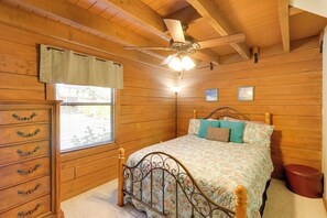 A wooden-paneled bedroom with a bed, dresser, ceiling fan, and window with curtains. - Boat, Fish & Swim: Lakefront Cabin in Okeechobee! (Okeechobee)