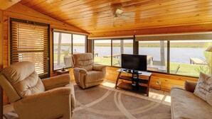 A cozy room with a wooden ceiling, large windows, a TV, and comfortable seating. - Boat, Fish & Swim: Lakefront Cabin in Okeechobee! (Okeechobee)