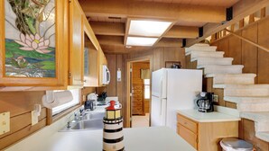 A kitchen with wooden cabinets, a white countertop, a stainless steel sink, a white refrigerator, and a staircase with white carpeted steps. - Boat, Fish & Swim: Lakefront Cabin in Okeechobee! (Okeechobee)