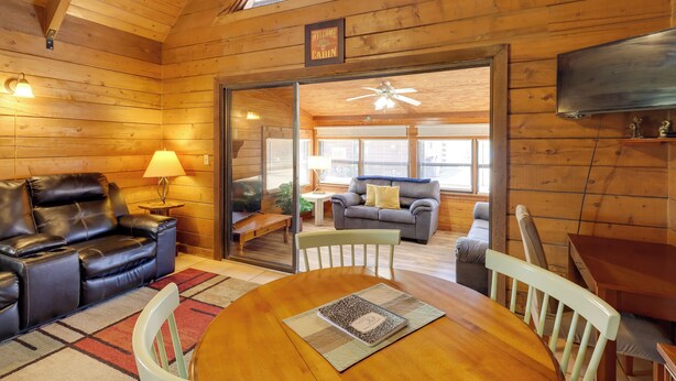 A cozy cabin interior with a wooden ceiling, a leather sofa, a dining table with chairs, and a television mounted on the wall. - Cabin w/ Boat Launch & Pool Access in Okeechobee (Okeechobee)