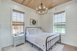 A bedroom with a bed, a nightstand, a chandelier, and two windows with blinds. - Contrell Cottage On Farm w/ Peaceful Views (Forest)