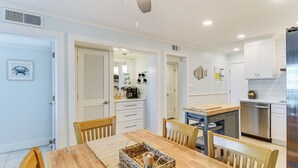 Una cocina moderna con armarios blancos, lavavajillas de acero inoxidable y una mesa de comedor de madera con sillas.