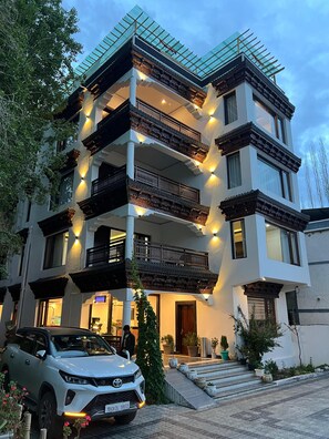 Un immeuble à plusieurs étages doté de balcons, avec une voiture garée devant et des plantes en pot.