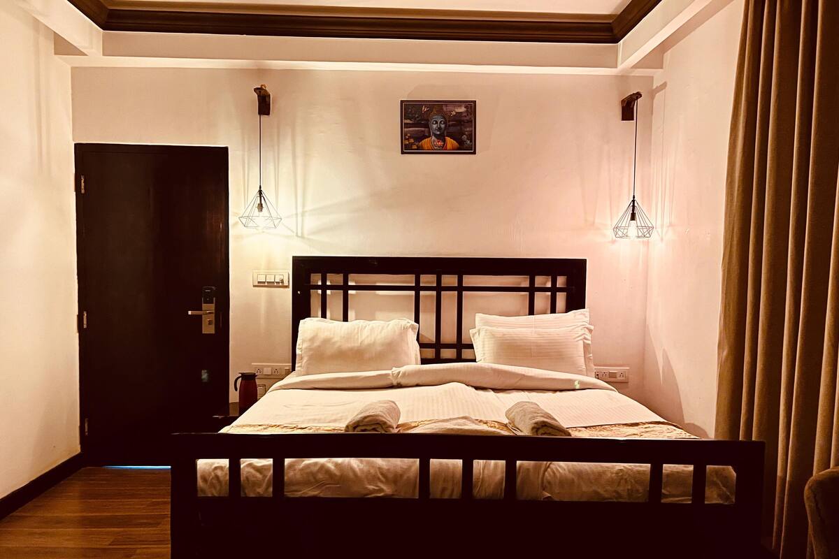 Una cama bien tendida con sábanas blancas en una habitación con suelo de madera y cabecero oscuro.
