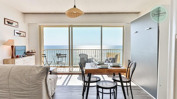 A balcony with a table set for dining, a sofa, and a TV on a stand.