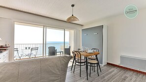 Une chambre avec un balcon, une table à manger avec des chaises, un lit et une grande fenêtre.