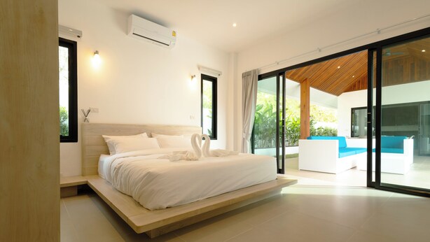 A modern bedroom with a large bed, built-in bench, and a view of an outdoor seating area. - Samui Paradise Pool Villa by Sea N' Rent (Koh Samui)