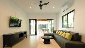 A modern living room with a flat-screen TV, a ceiling fan, and a large window. - Samui Paradise Pool Villa by Sea N' Rent (Koh Samui)