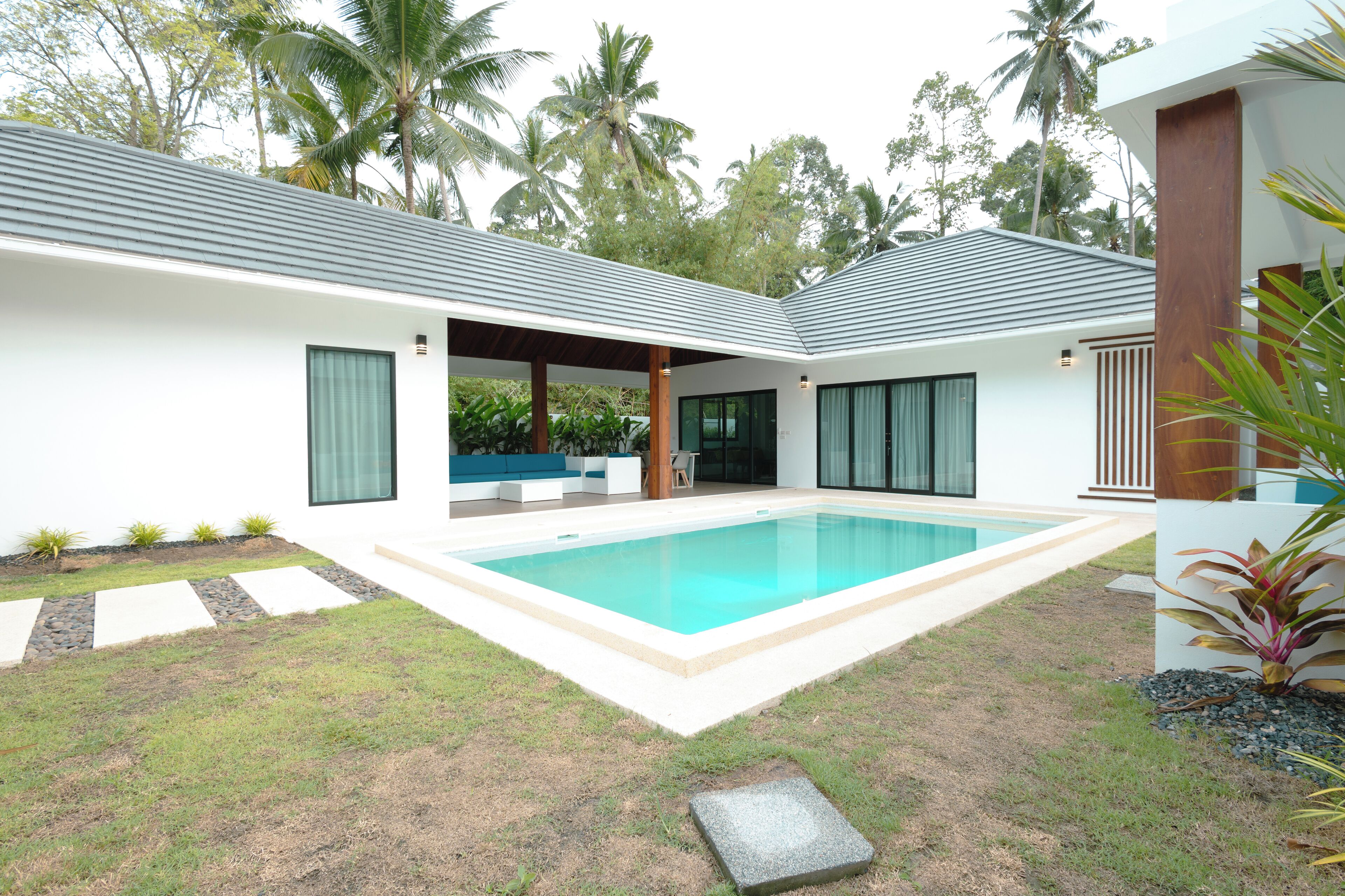 A modern house with a swimming pool, covered patio, and lush greenery.