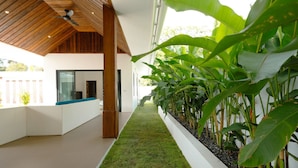 A modern interior with a long corridor lined with large green plants, a wooden ceiling, and a white bench area. - Samui Paradise Pool Villa by Sea N' Rent (Koh Samui)