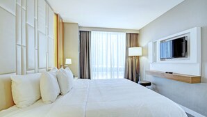 A hotel room with a large bed, a TV mounted on the wall, and a window with curtains.