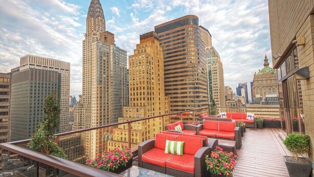 A rooftop terrace with outdoor seating, city skyline views, and potted plants.