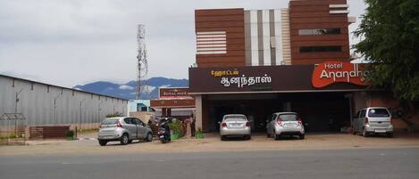A hotel named 'Hotel Anandha' with a modern design, featuring a prominent signboard and a parking area with several cars.
