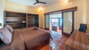 A bedroom with a bed, a ceiling fan, a desk, and a sliding glass door leading to a balcony. - Villa Cemara  (Ceningan Island)