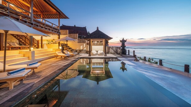 A serene infinity pool with a wooden deck and lounge chairs, overlooking a calm sea at sunset. - Villa Cemara  (Ceningan Island)