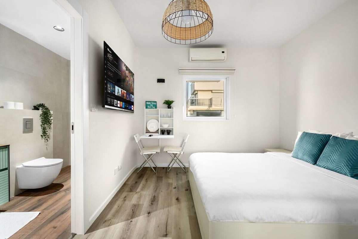 A modern bedroom with a large bed, a desk, and a view of the city through a window.