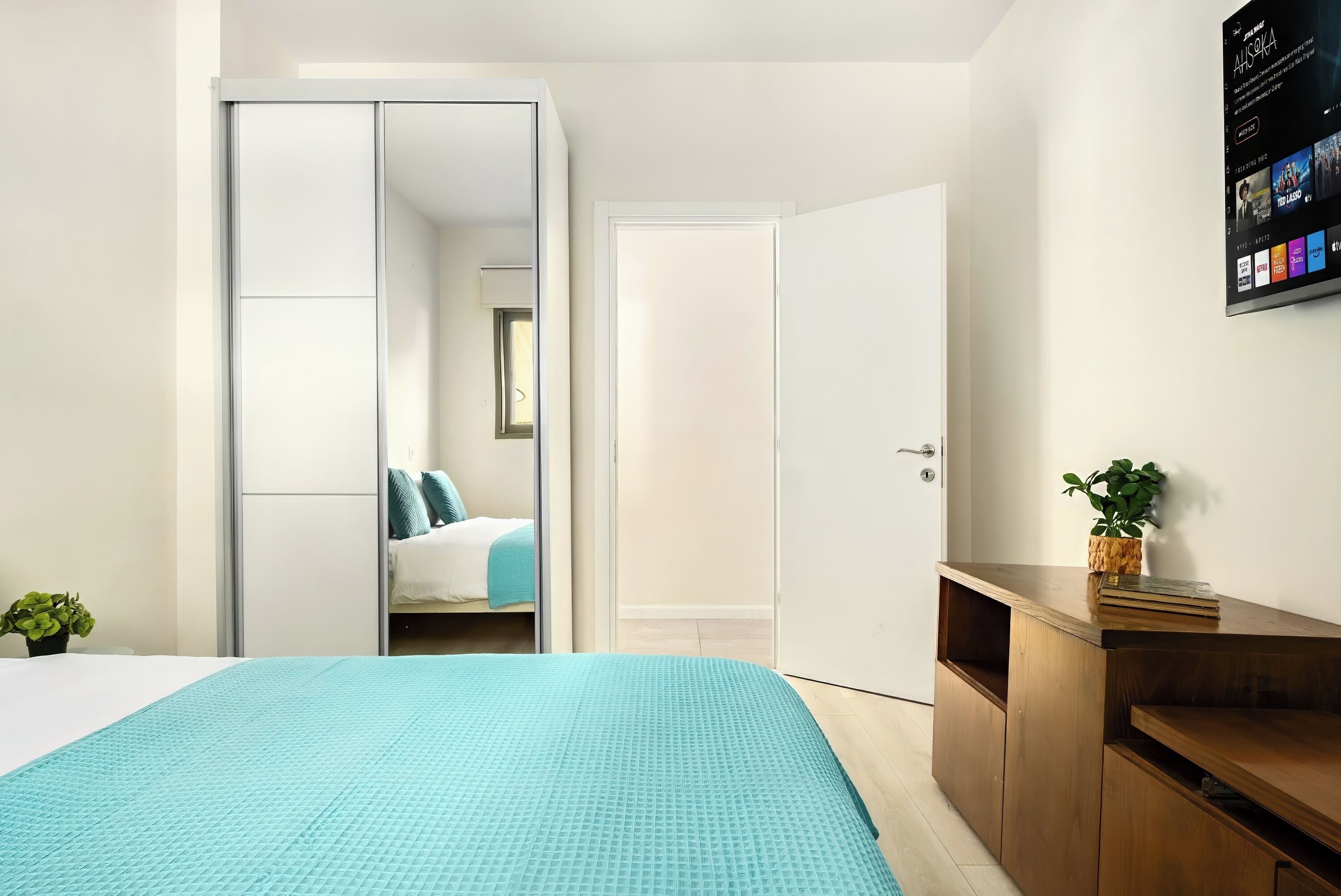 Une chambre à coucher moderne avec un lit, une armoire et un téléviseur fixé au mur.