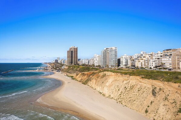 A coastal cityscape with a sandy beach, high-rise buildings, and a clear blue sky. - Netanya Beach Pool Studio by Sea N' Rent (Netanya)