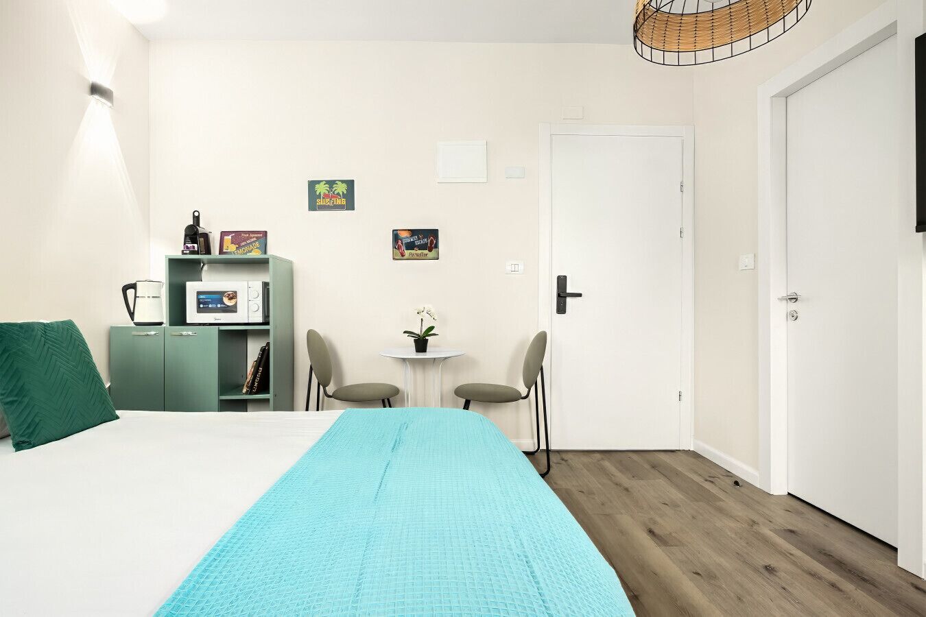 Une chambre à coucher avec un lit, une armoire verte, une petite table avec des chaises et une porte.