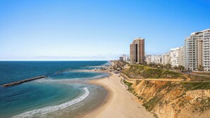 A coastal cityscape with a sandy beach, a rocky breakwater, and high-rise buildings. - Netanya Beach Pool Studio by Sea N' Rent (Netanya)