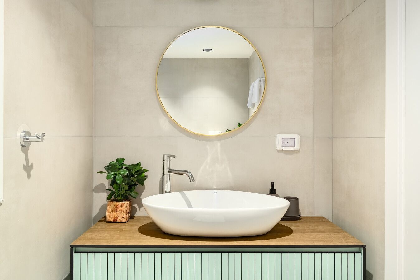 Ein modernes Badezimmer mit einem runden Spiegel, einem weißen Waschbecken und einer Holz-Kommode.