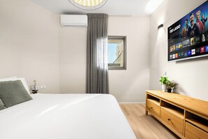 Une chambre d’hôtel moderne avec un grand lit, une commode en bois, un téléviseur à écran plat fixé au mur et une fenêtre donnant sur la ville.