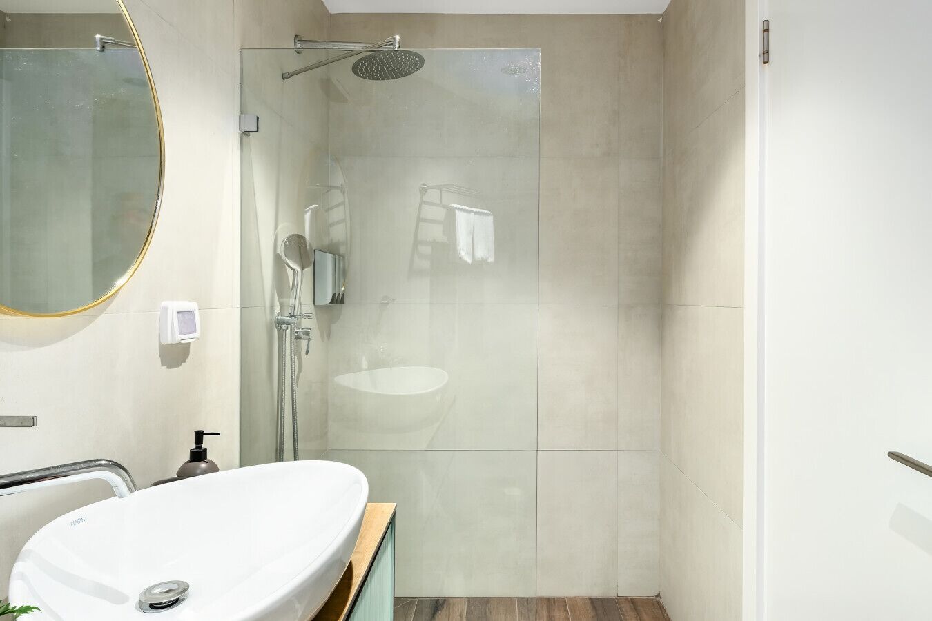Un baño moderno con ducha envuelta en vidrio, un lavabo blanco y un espejo con marco dorado.