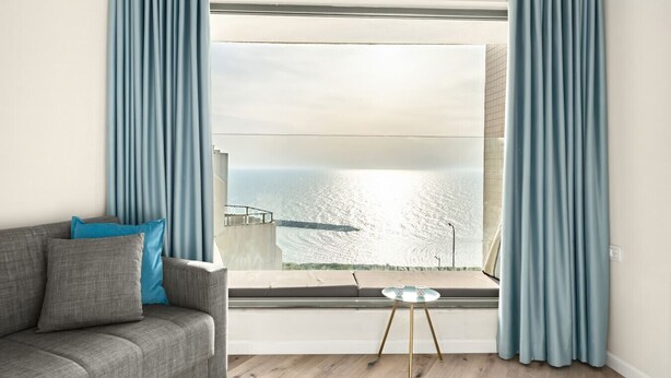 A modern living room with a grey sofa, a small round table, and a large window with a view of the sea. - Netanya Beach Pool Studio by Sea N' Rent (Netanya)
