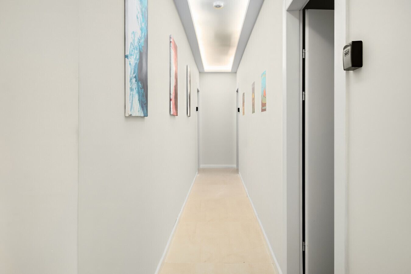 Um corredor moderno com paredes claras, piso de madeira e várias obras de arte emolduradas.