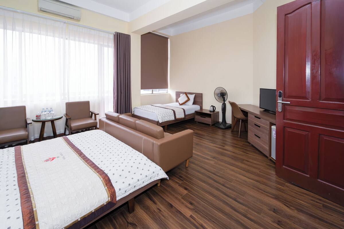 Une chambre d’hôtel avec deux lits, un bureau, une chaise, une petite table avec des bouteilles d’eau et un téléviseur.