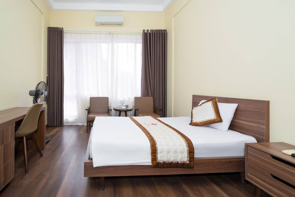 Une chambre d’hôtel avec un grand lit, un bureau, une chaise, une petite table et une table de chevet.