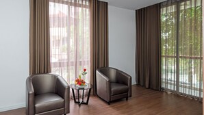 Una habitación amplia con dos sillones de cuero, una mesita de cristal con un centro de mesa floral y ventanas grandes con cortinas translúcidas.