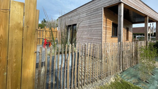 Une maison moderne avec une façade en bois, une cour clôturée et un porche abrité.