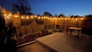 Un espace patio agrémenté d’une clôture en bois, de guirlandes lumineuses, d’une table et de chaises.