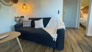Un canapé bleu foncé, un plaid blanc, une petite table ronde et un luminaire suspendu.